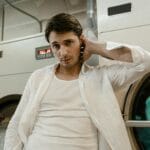 Młody mężczyzna w białej koszuli oparty o pralkę w pralni samoobsługowej