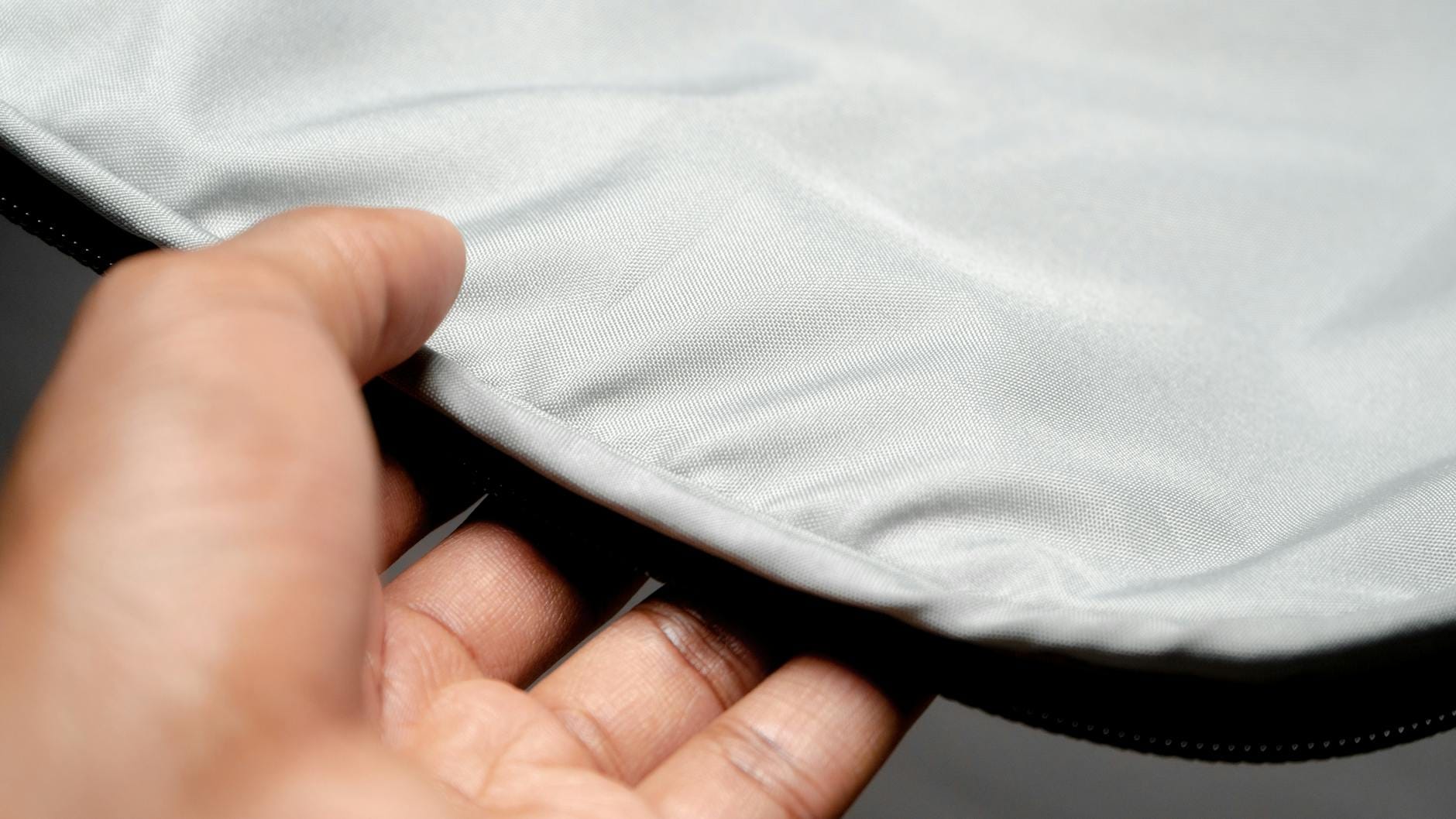 Jak rozpoznać perełki w Uniqlo: materiały, szwy, detale Dłoń ściskająca biały materiał, widoczna faktura tkaniny Uniqlo