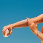 Kobieta na plaży nakłada kosmetyk na ramię w słoneczny dzień