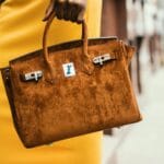 Kobieta z elegancką brązową torebką Hermès na tle miejskiej ulicy