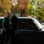 Młoda kobieta w futrze Hermès przy klasycznym aucie jesienią