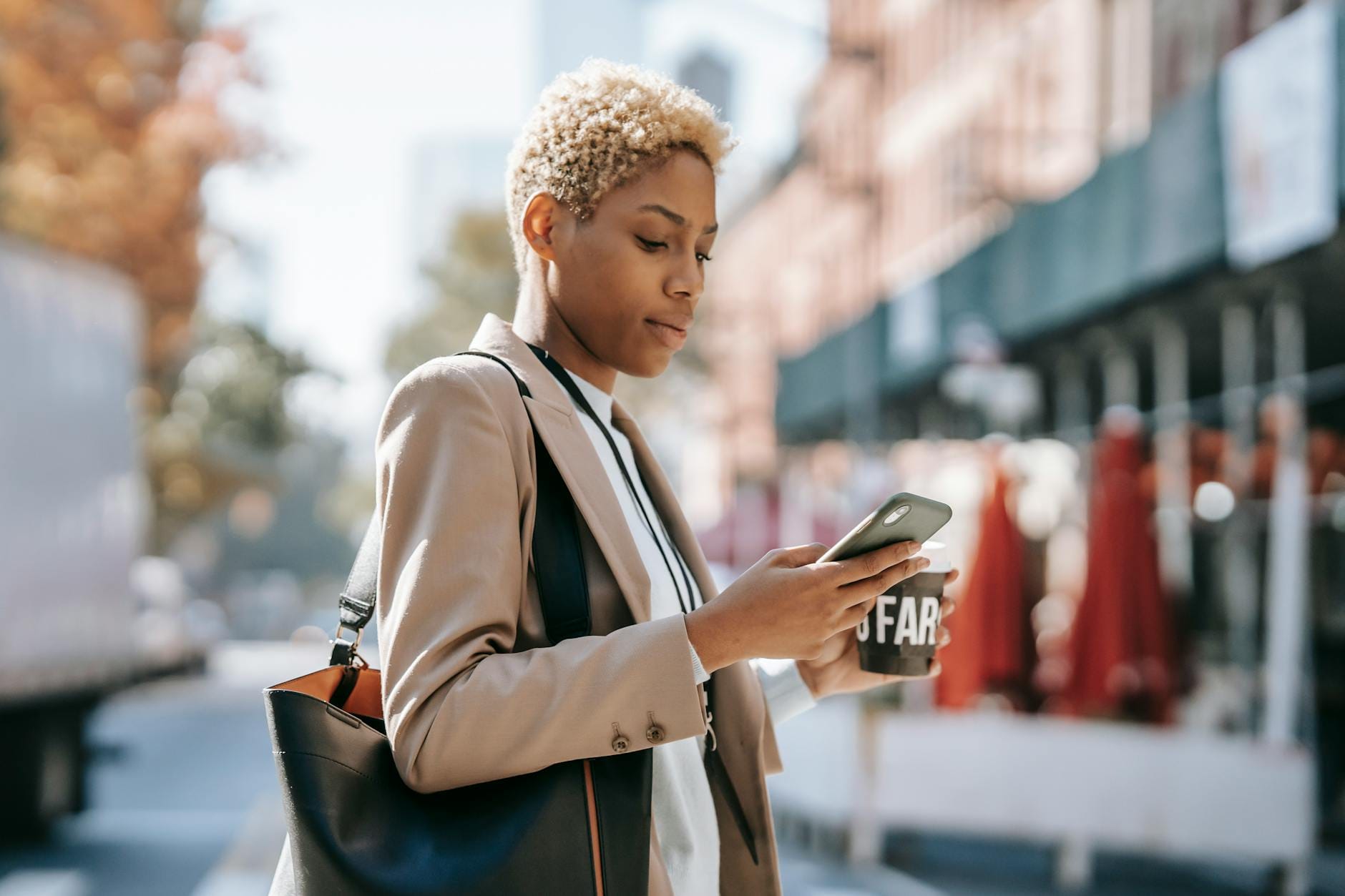 Młoda kobieta z telefonem i kawą przechodzi przez ulicę Młoda kobieta z telefonem i kawą przechodzi przez ulicę