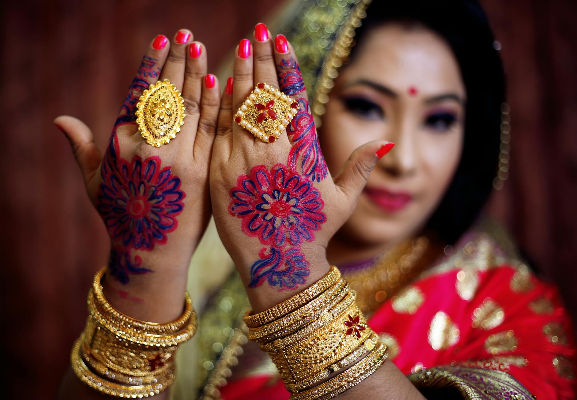 Panna młoda prezentuje złotą biżuterię i zdobione henną dłonie