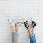 Uniesione stopy w modnych sneakersach i dżinsach na tle białej ceglanej ściany