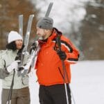 Uśmiechnięta para w zimowych kurtkach trzyma narty na śniegu