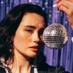 Brunetka w stylowym dresie Adidas pozuje z lustrzaną dyskotekową kulą