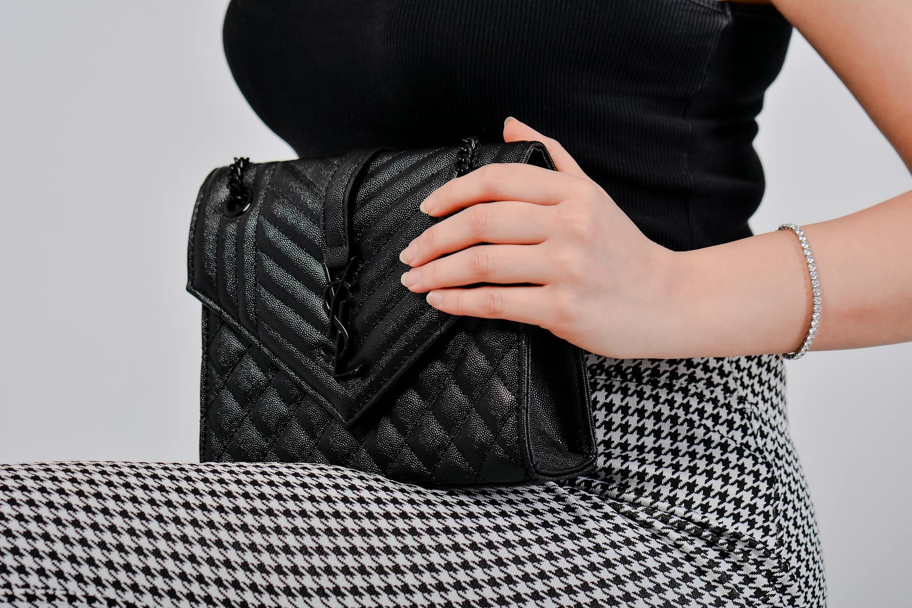 Kobieta z czarną pikowaną torebką na tle sukienki w pepitkę