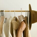 Beżowe i brązowe ubrania H&M na wieszaku, ręka wybiera jedną sztukę
