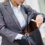 Kobieta w marynarce w kratę zagląda do skórzanej torebki Saint Laurent