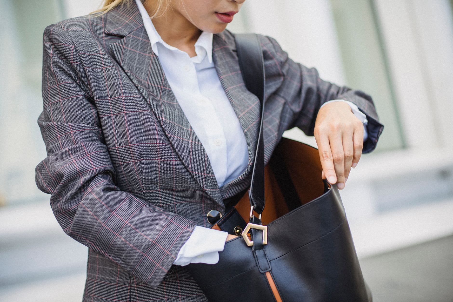 Torebka Saint Laurent Sac de Jour: dla kogo jest ten model i jak go nosić? Kobieta w marynarce w kratę zagląda do skórzanej torebki Saint Laurent