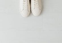Białe sneakersy na jasnej drewnianej podłodze