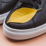 Czarne skórzane sneakersy z żółtym liściem na pastelowym tle