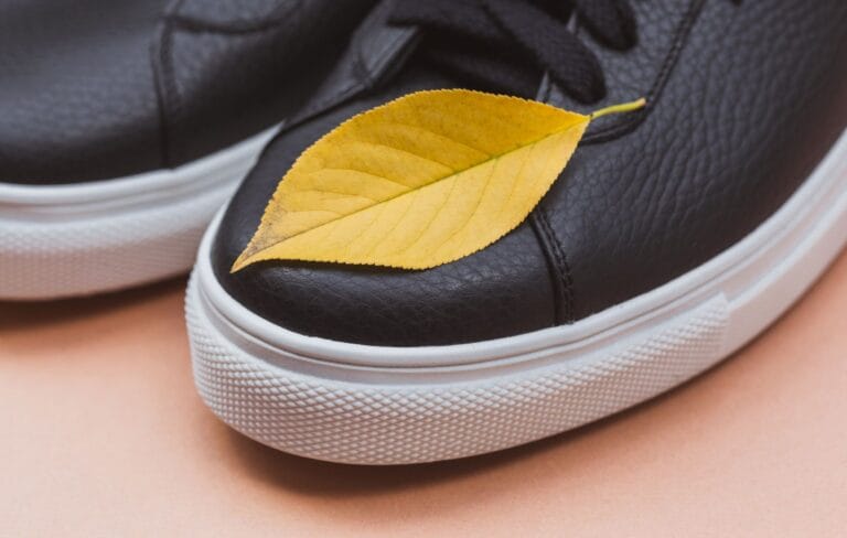 Czarne skórzane sneakersy z żółtym liściem na pastelowym tle